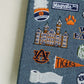 Hardcover navy blue notebook with various Auburn University icons embroidered on the front.