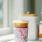 Light pink coffee sleeve with watercolor Taylor Swift inspired symbols.