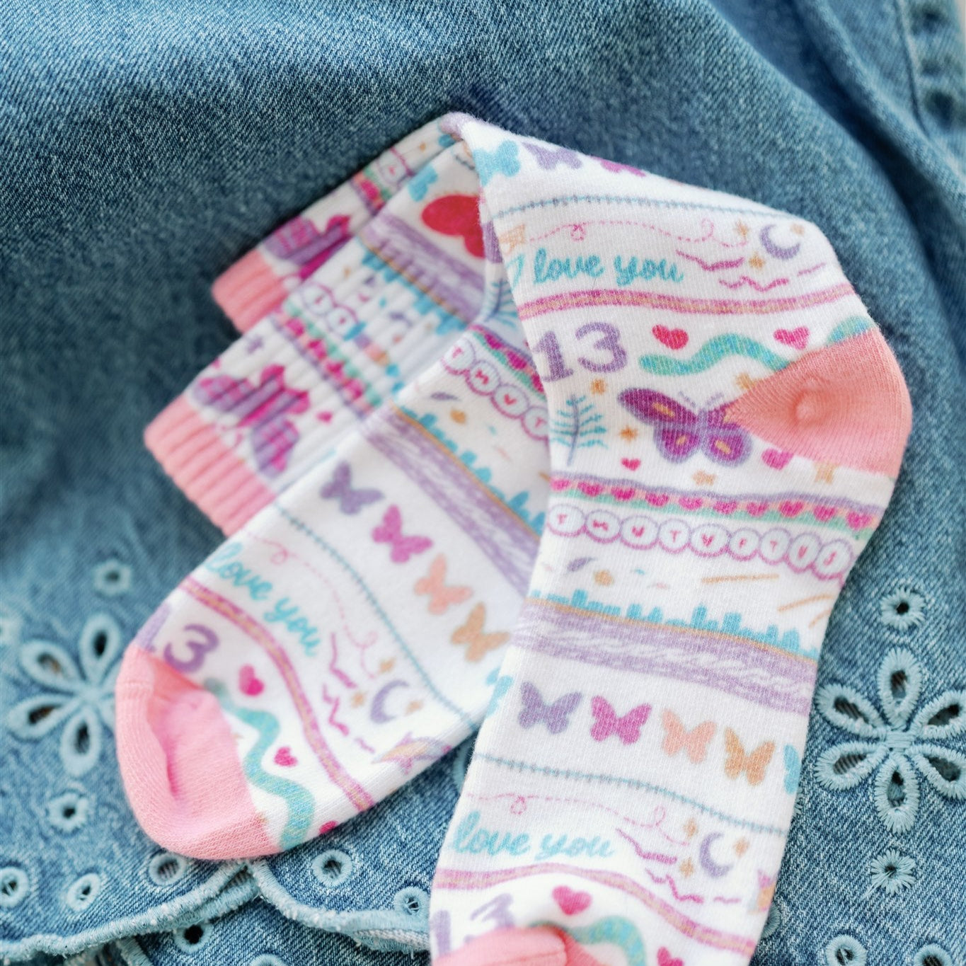 White socks with colorful pattern of butterflies and other Taylor Swift symbols.