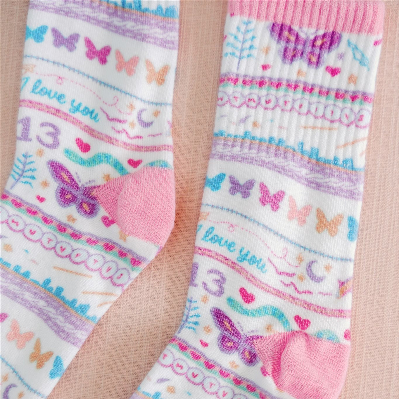 White socks with colorful pattern of butterflies and other Taylor Swift symbols.