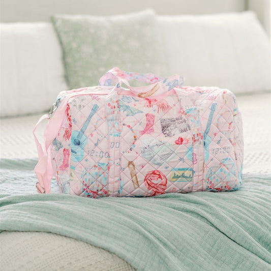 Light pink quilted duffle with 2 handles, a strap, and a pattern featuring original watercolor art of Taylor Swift icons.