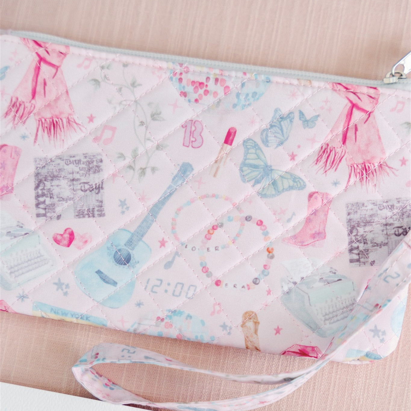Light pink quilted wristlet with watercolor Taylor Swift symbols as the pattern.
