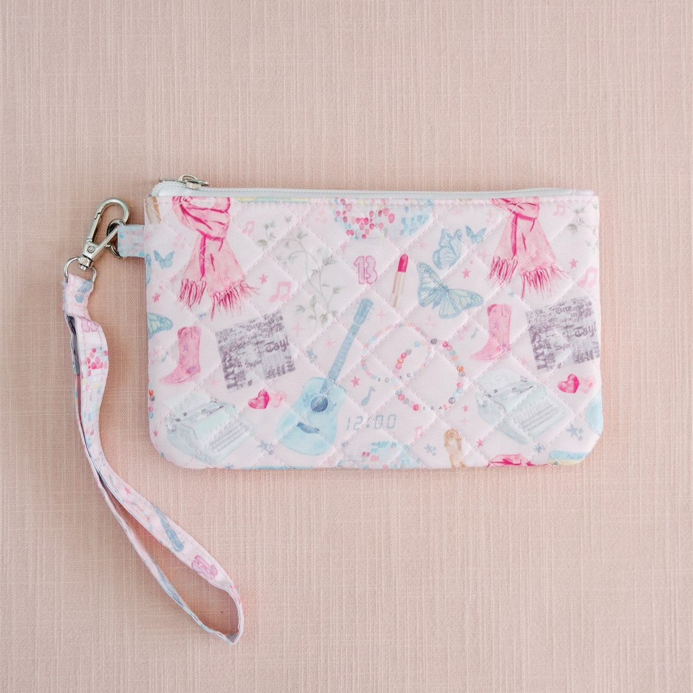 Light pink quilted wristlet with watercolor Taylor Swift symbols as the pattern.