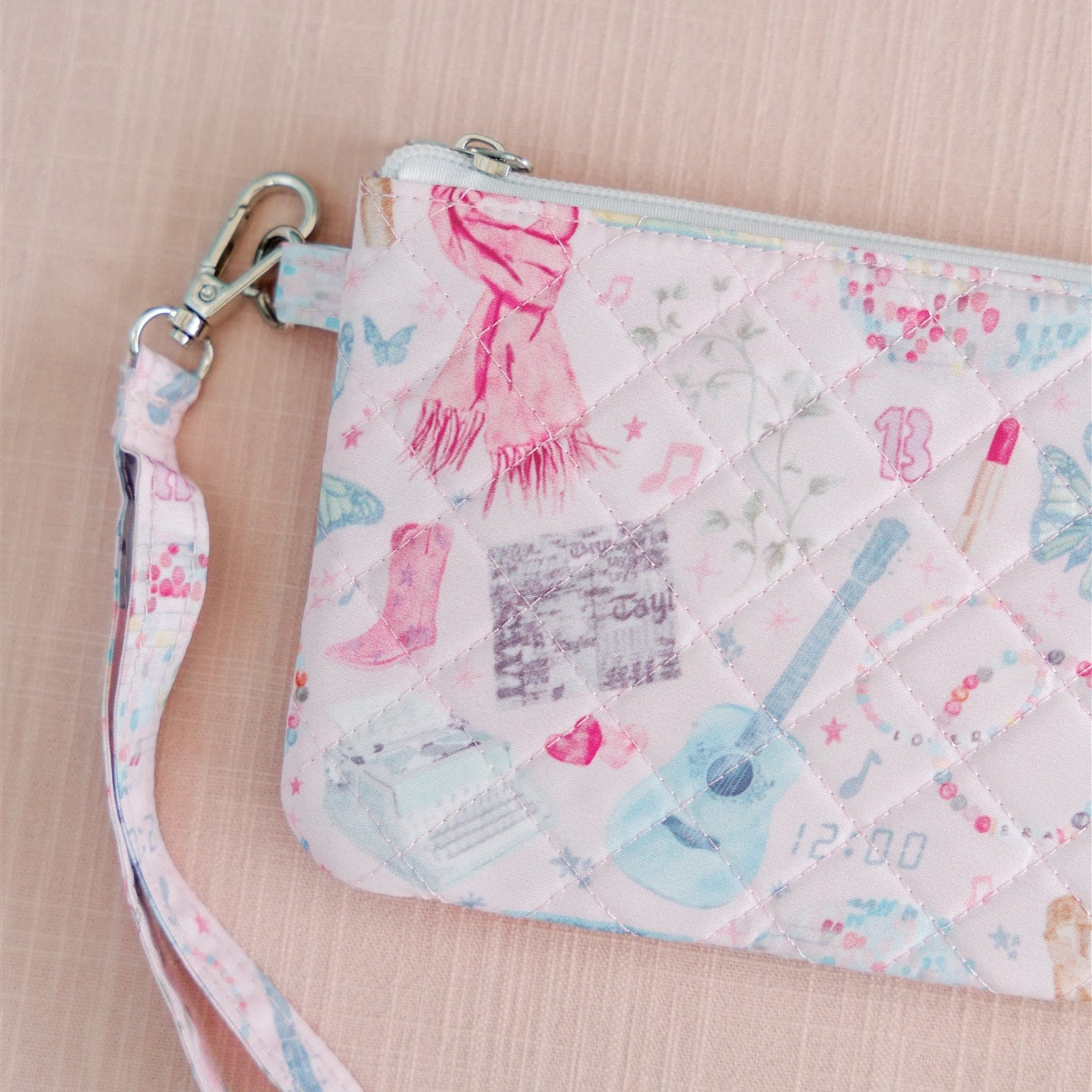 Light pink quilted wristlet with watercolor Taylor Swift symbols as the pattern.