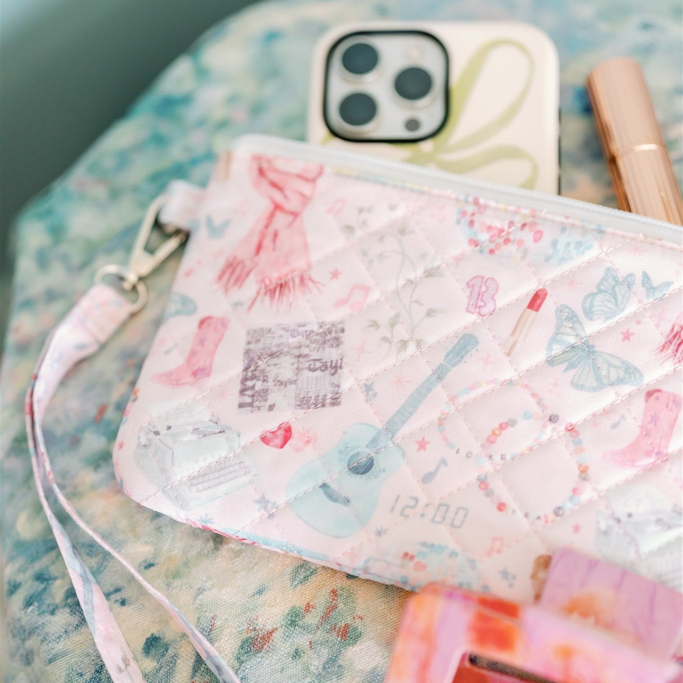 Light pink quilted wristlet with watercolor Taylor Swift symbols as the pattern.