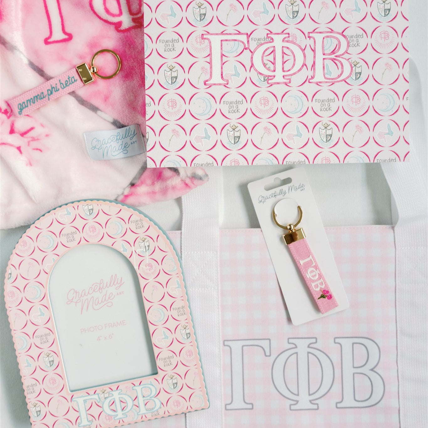 Gamma Phi Beta themed items including a pink keychain, tote bag, and decorative items on a matching pink and white patterned background.
