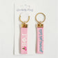 Front and back of a pink keychain with Gamma Phi Beta embroidered on it with Gracefully Made Art branded packaging