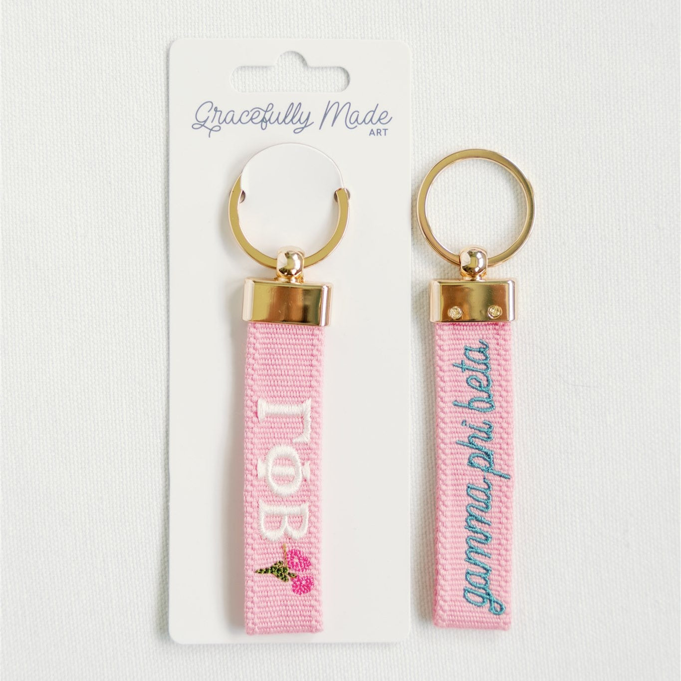 Front and back of a pink keychain with Gamma Phi Beta embroidered on it with Gracefully Made Art branded packaging