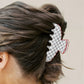 Person with a grey and white checkered hair clip in their bun against a plain background