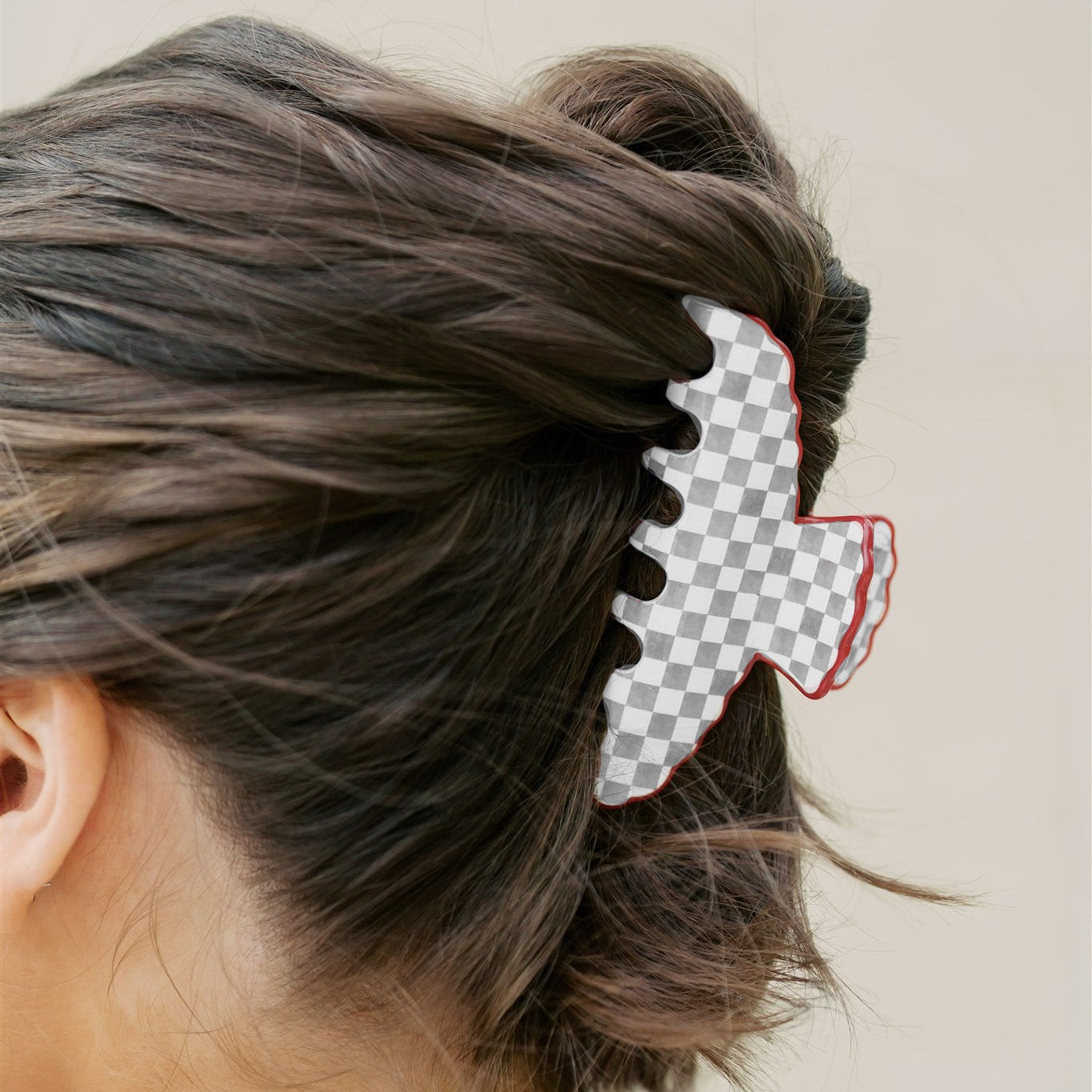 Person with a grey and white checkered hair clip in their bun against a plain background