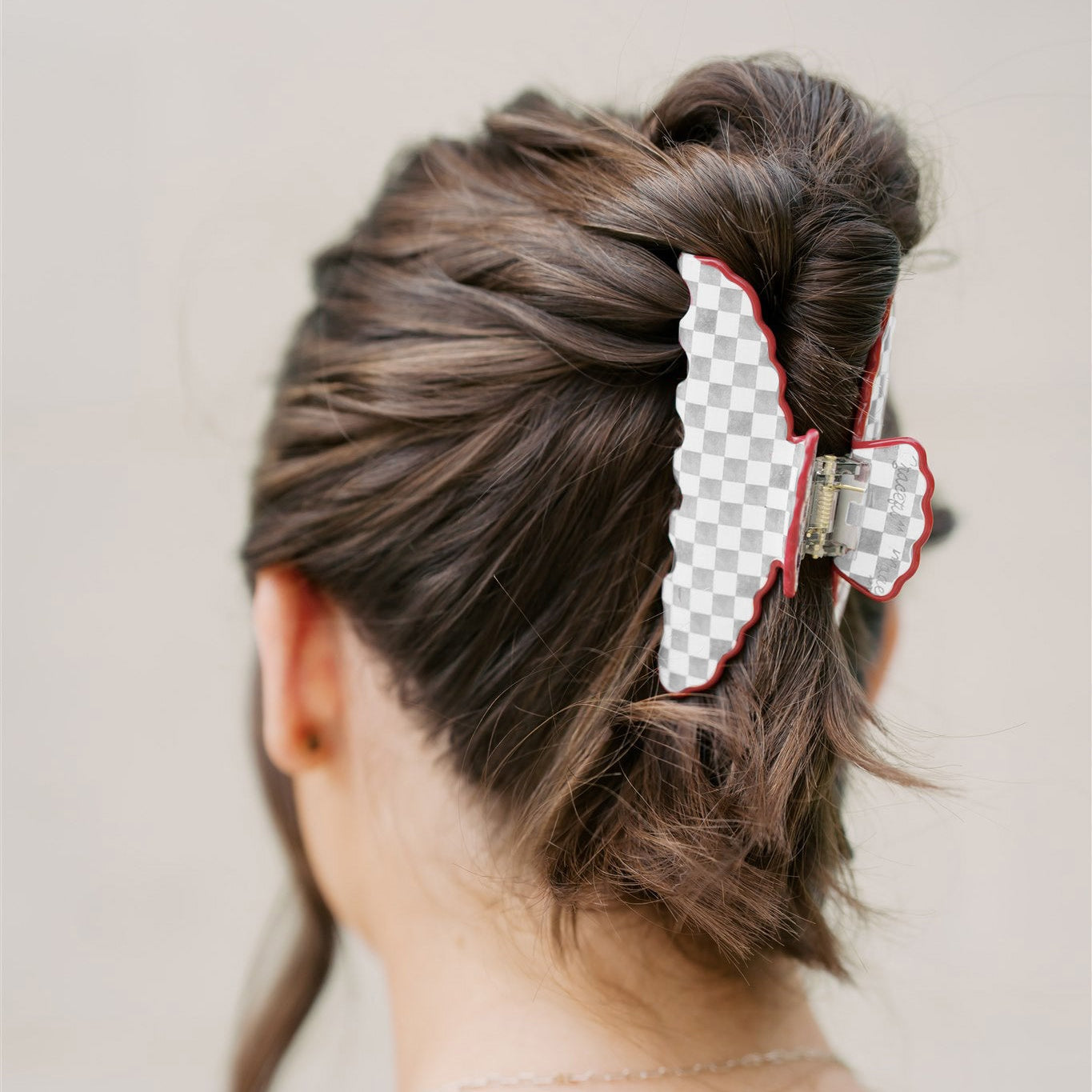Person with a grey and white checkered hair clip in their hair against a plain background