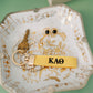 Decorative dish with keys, a bracelet, and a yellow keychain with Kappa Alpa Theta Greek letters embroidered on it