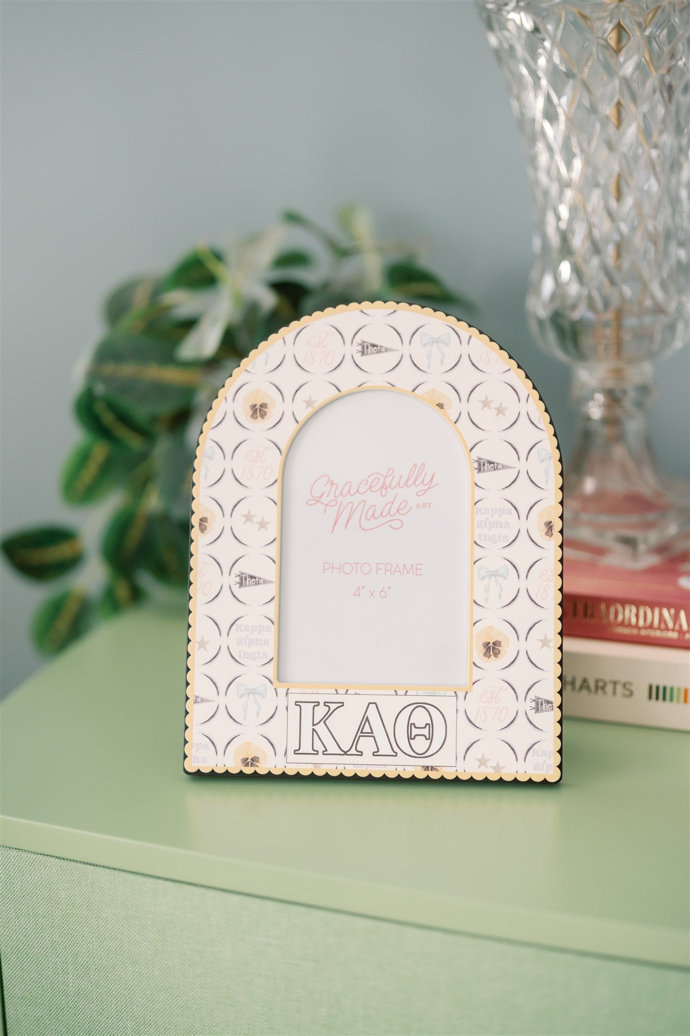 Decorative photo frame with Kappa Alpha Theta pattern and Greek letters on a green dresser.