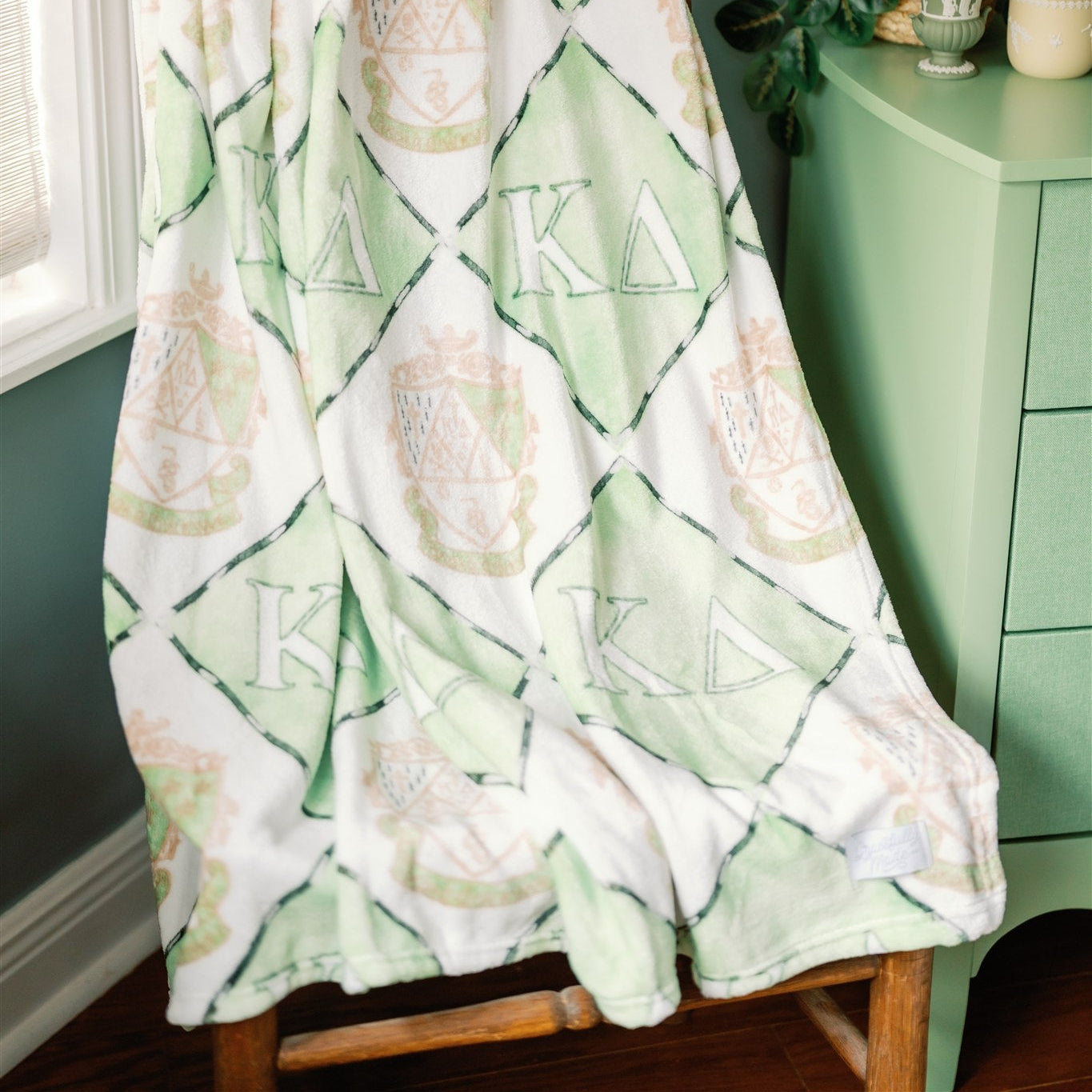 Green and white Kappa Delta patterned blanket draped over a chair in a room with green walls.