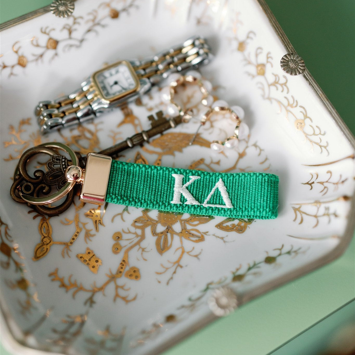 Green keychain with Kappa Delta Greek letters embroidered in white on a jewelry dish.