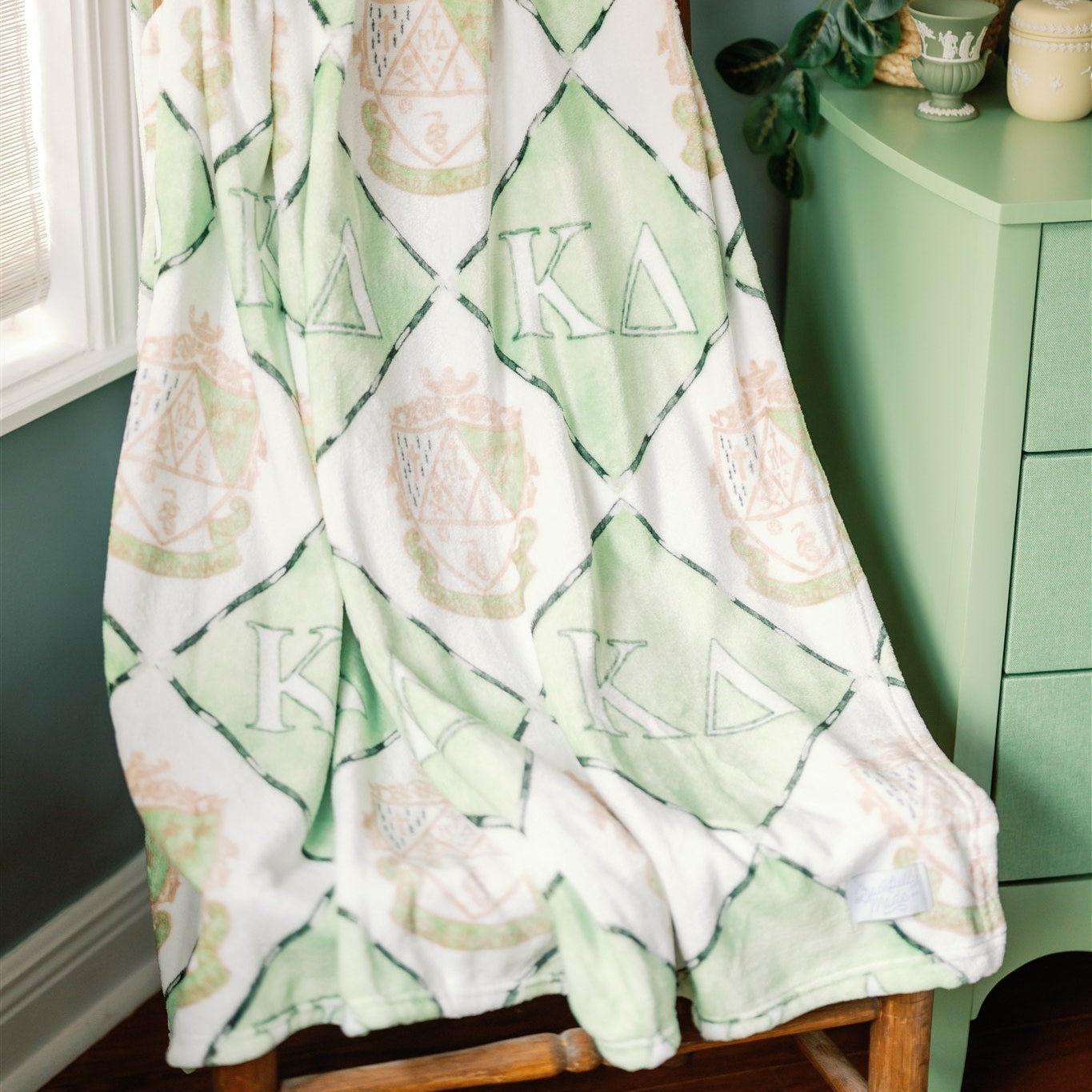 Blanket with Kappa Delta Greek letter symbols draped over a chair in a room with green walls.