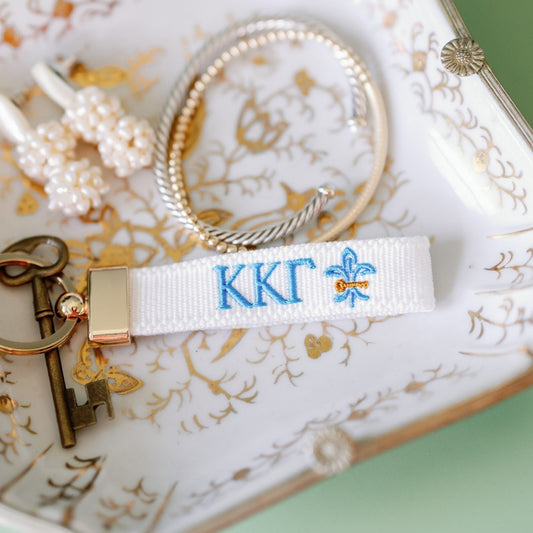 White keychain with 'KKG' logo on a decorative plate with jewelry.