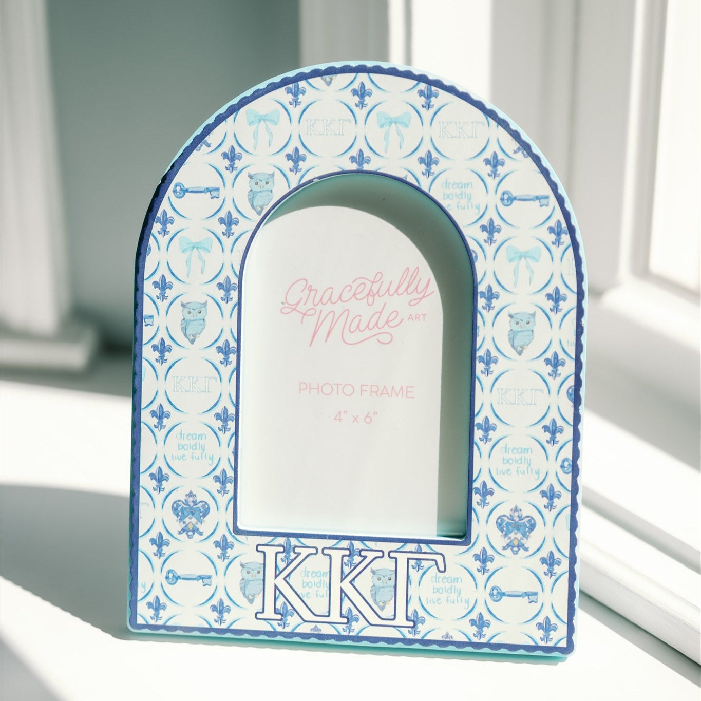 Decorative arch-shaped frame with blue patterns and Kappa Kappa Gamma Greek letters on a neutral background
