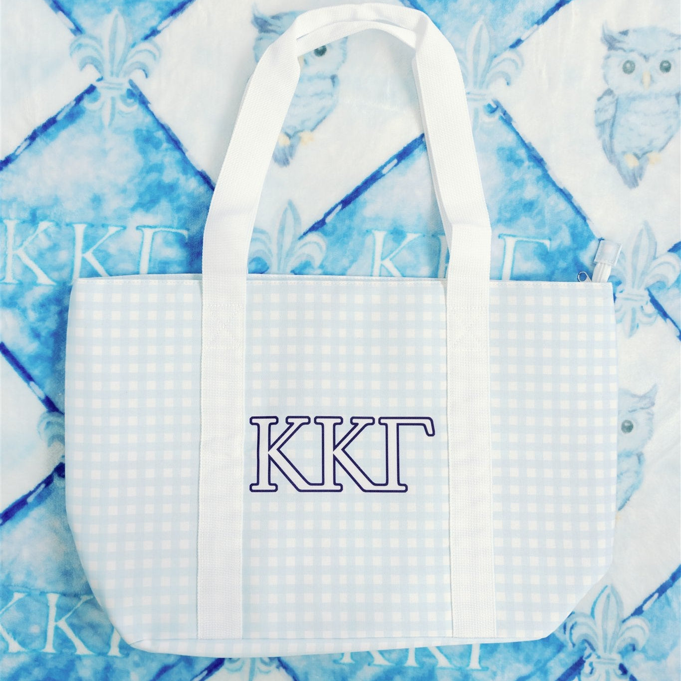 Blue gingham tote bag with KKG Greek letters and white straps on a blue background.