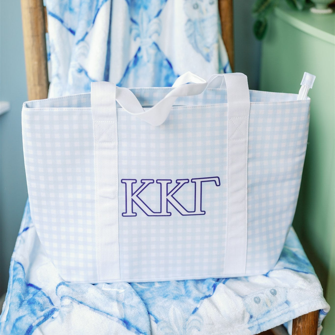 White bag with 'KKG' monogram on a chair with blue and white patterned blanket