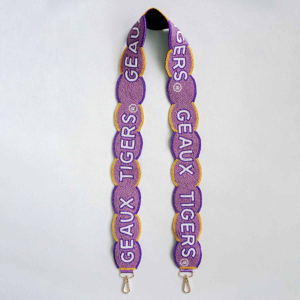Purple and gold beaded shoulder strap with 'GEAUX TIGERS' text, featuring gold metal clips at the bottom, shown against a light gray background.