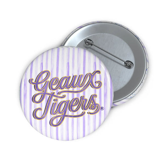 Two round pinback buttons showing the front and back. The front button has a white background with light purple vertical stripes and the words 'Geaux Tigers' in purple cursive with a gold outline.