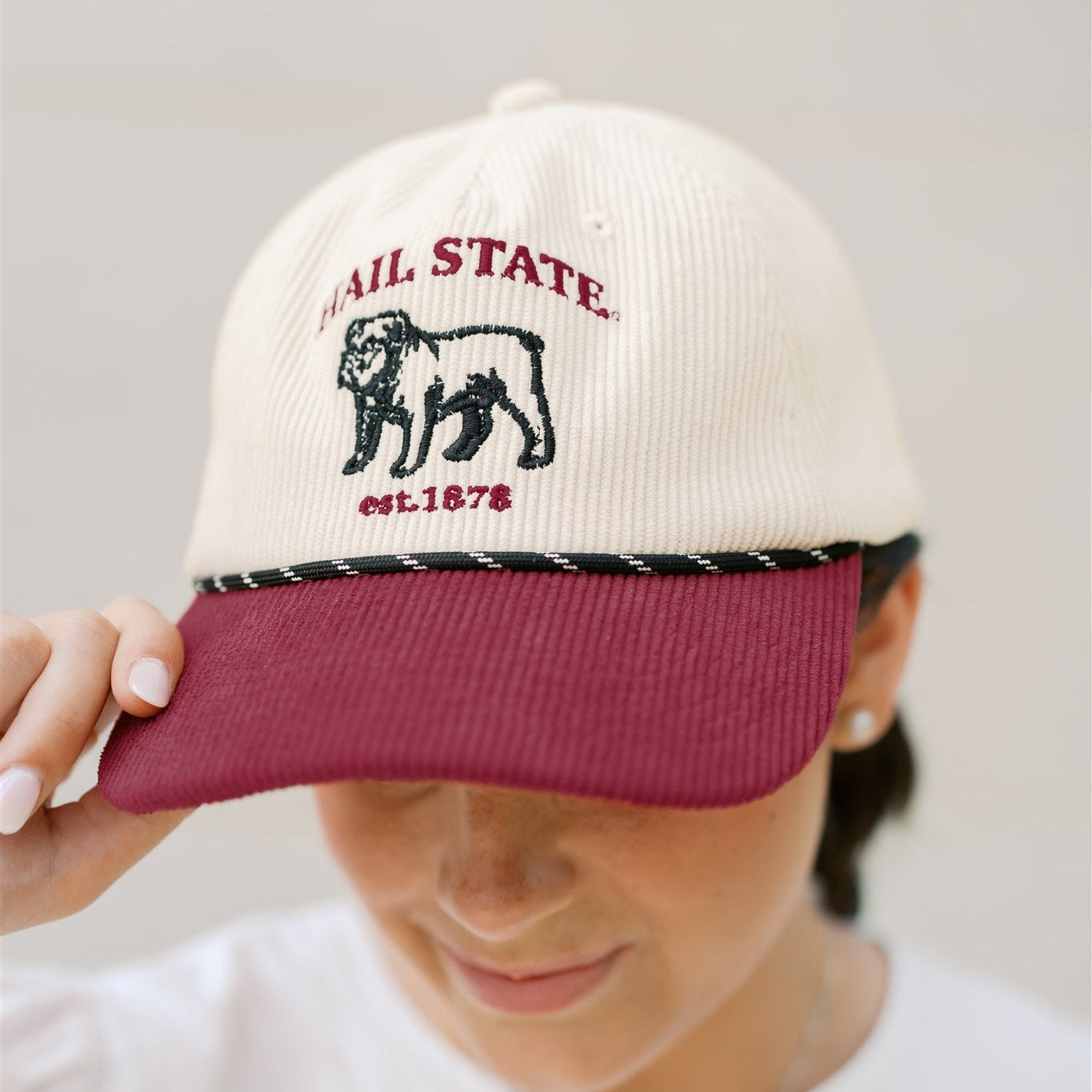Person wearing a cap with 'Hail State' and bulldog logo on a plain background