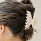 Person with hair styled in a bun using a decorative orange hair clip on a plain background