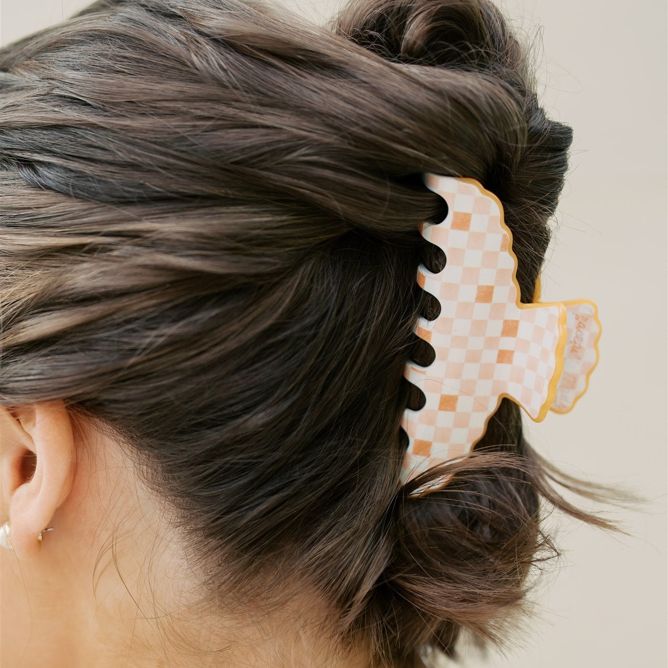 Person with hair styled in a bun using a decorative orange hair clip on a plain background