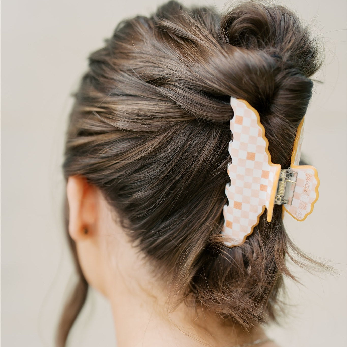 Back view of a person with styled hair featuring an orange decorative hair clip on a plain background