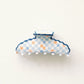 Decorative claw clip with an orange and blue checkered pattern and blue scalloped edge on a white background