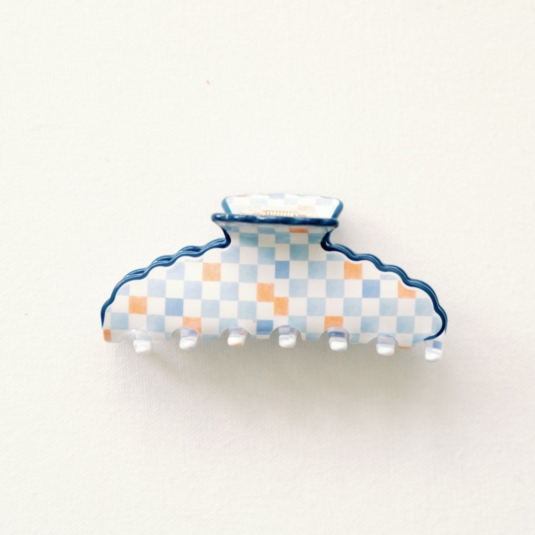 Decorative claw clip with an orange and blue checkered pattern and blue scalloped edge on a white background