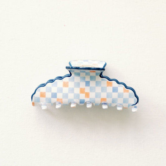 Decorative claw clip with an orange and blue checkered pattern and blue scalloped edge on a white background