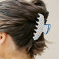 Woman with a bun wearing a blue and orange decorative claw clip on a plain background