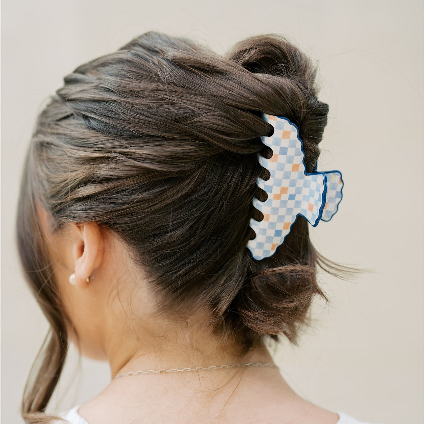 Person with a bun featuring a blue and orange checkered hair clip against a neutral background