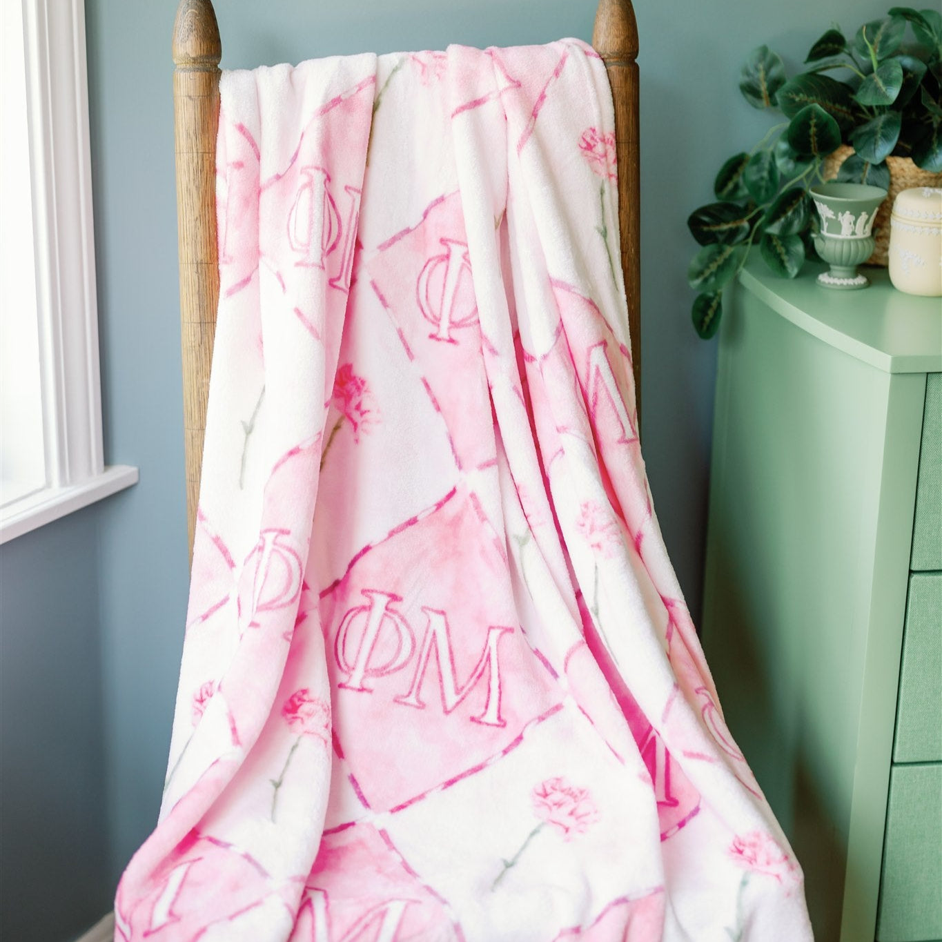 Pink and white Ph Mu patterned blanket draped over a wooden chair against a light blue wall.