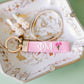Pink Phi Mu keychain with gold clasp on a decorative plate.