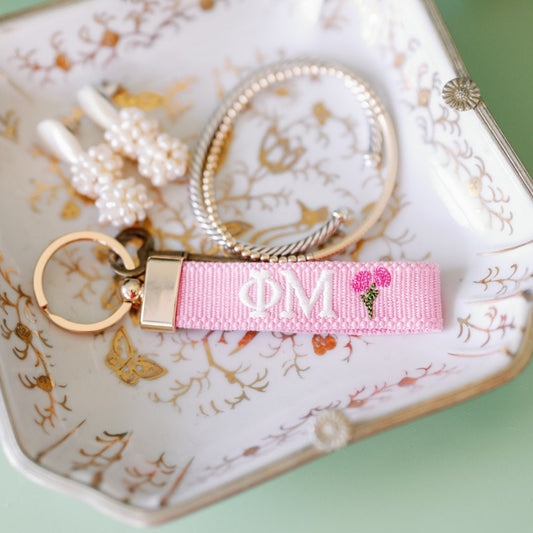 Pink Phi Mu keychain with gold clasp on a decorative plate.