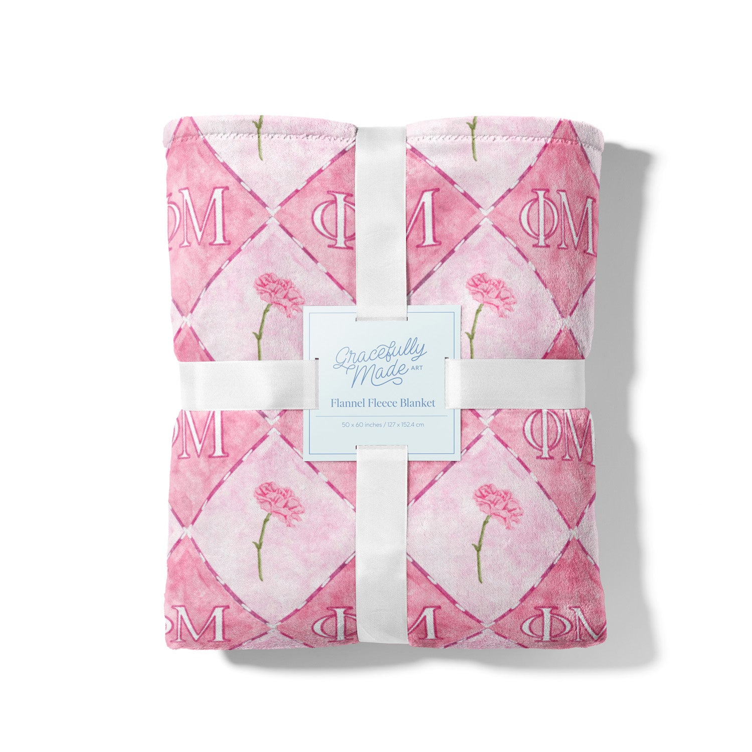Pink quilt with floral patterns and Phi Mu Greek letters, tied with a white ribbon on a white background.
