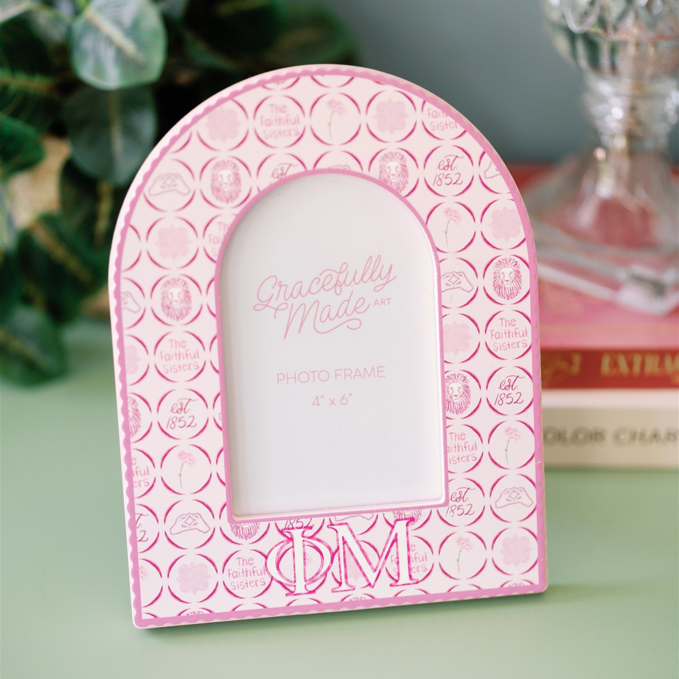 Pink photo frame with decorative patterns and Phi Mu Greek letters on a green surface