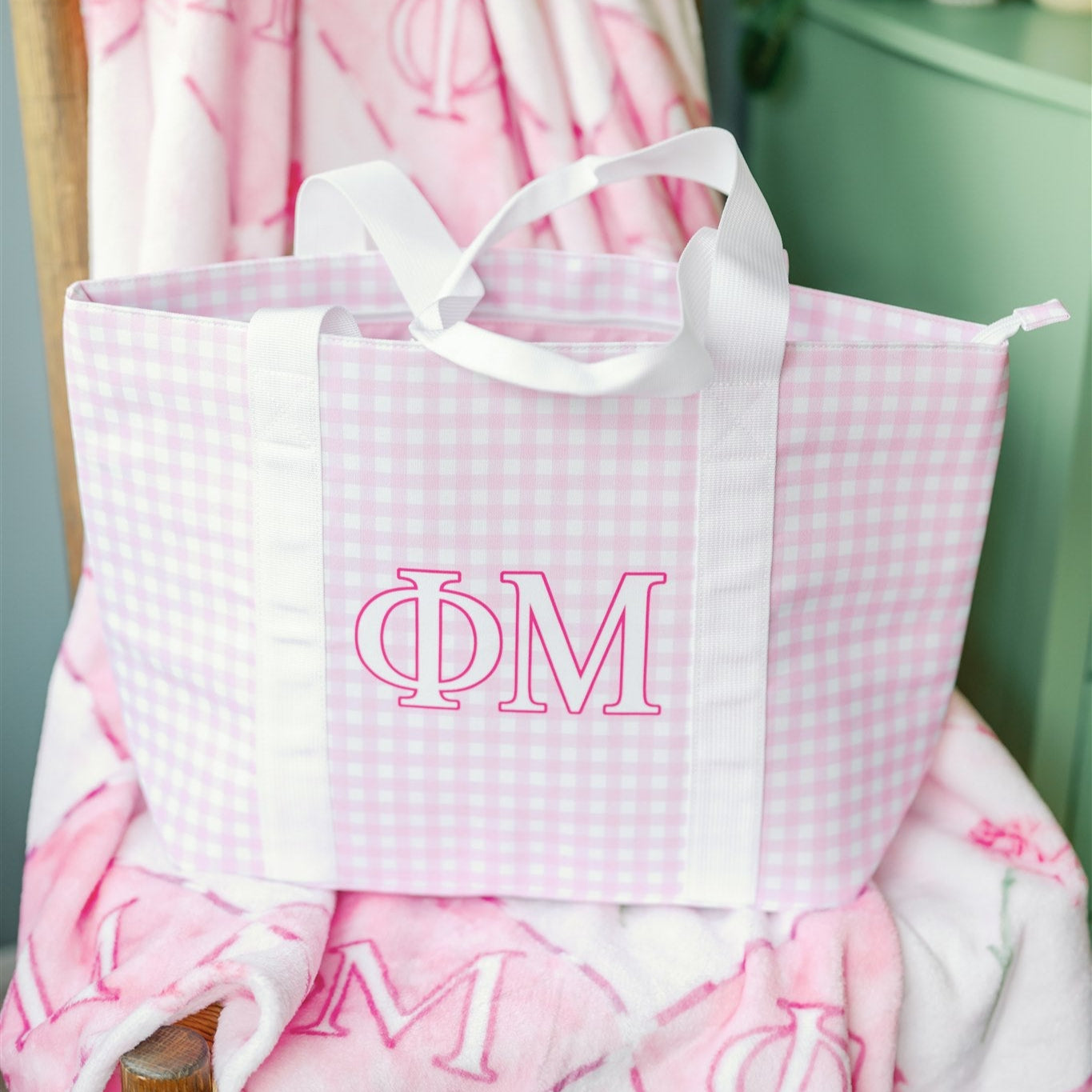Pink and white checkered bag with Phi Mu Greek letters on a chair with pink floral blanket