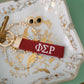 Red keychain with white Phi Sigma Rho Greek letters embroidered on it set on a decorative dish.