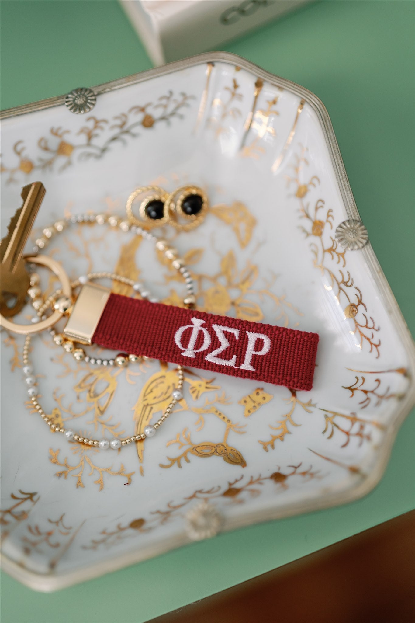 Red keychain with white Phi Sigma Rho Greek letters embroidered on it set on a decorative dish.