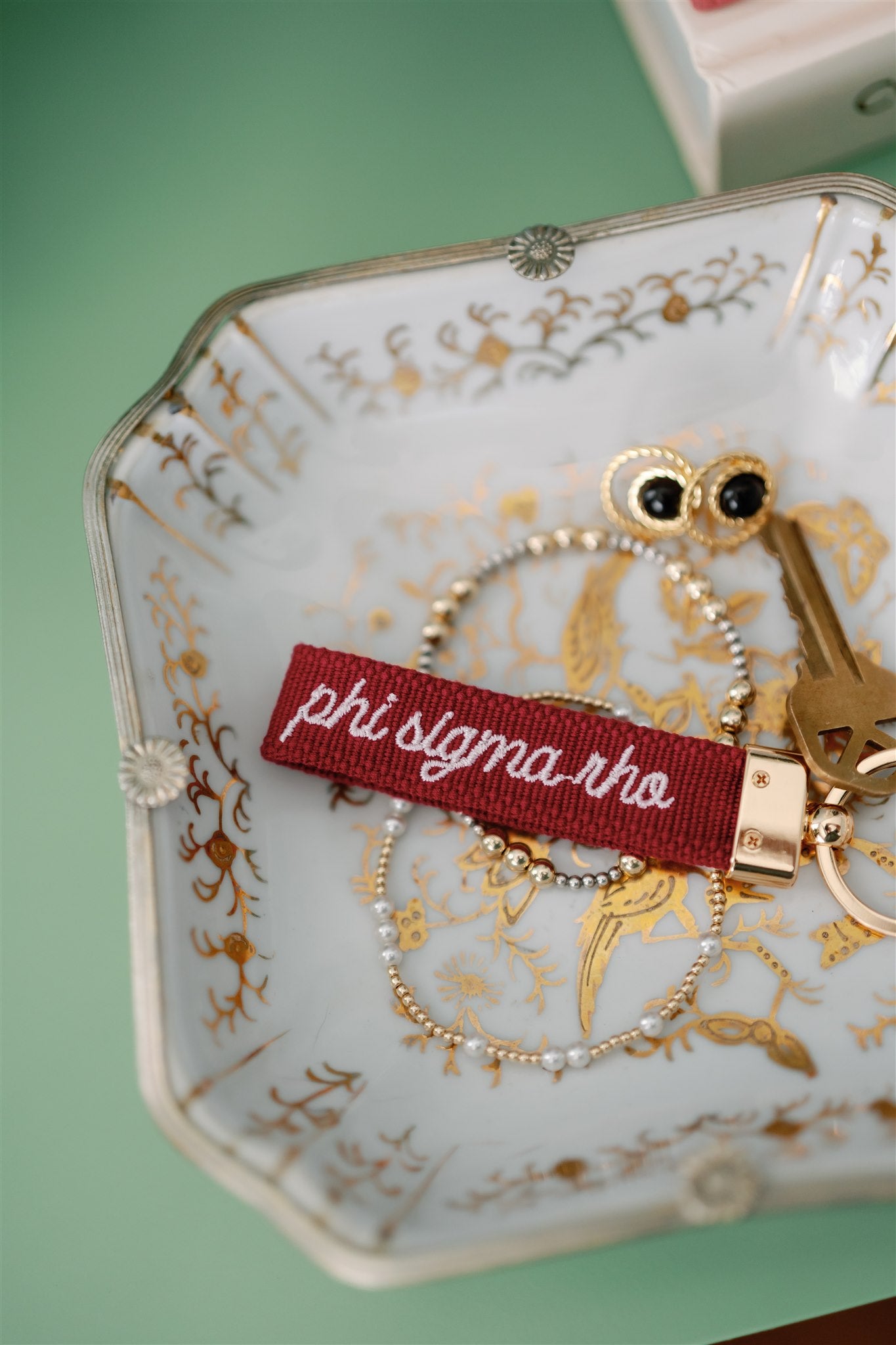Decorative dish with jewelry and a red 'phi sigma rho' embroidered keychain.