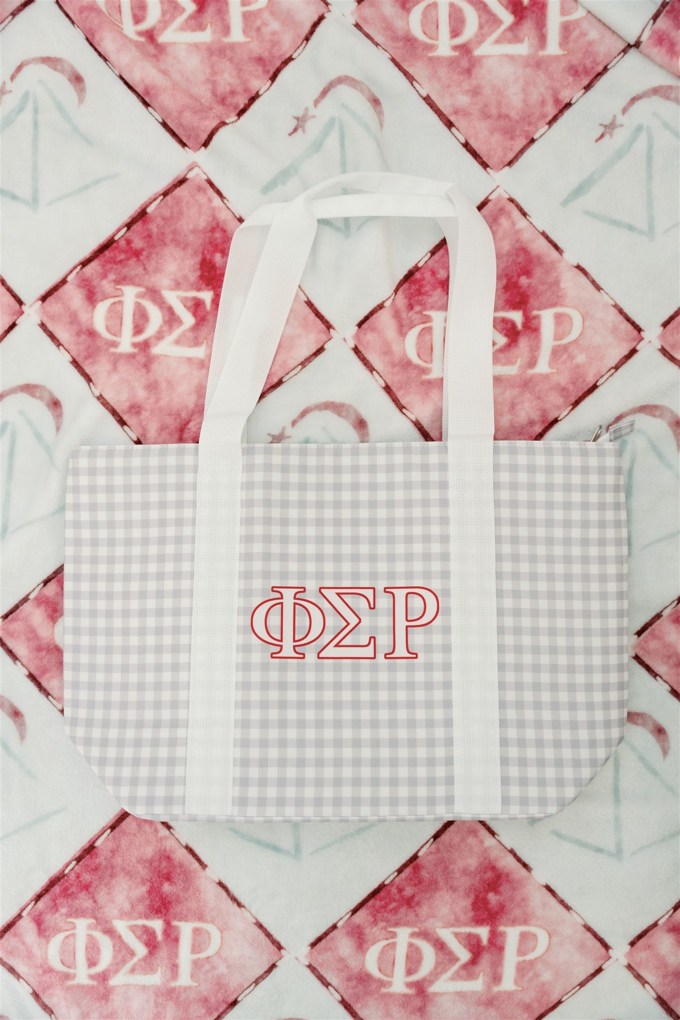 White and gray checkered tote bag with Phi Sigma Rho Greek letters on a red and gray blanket