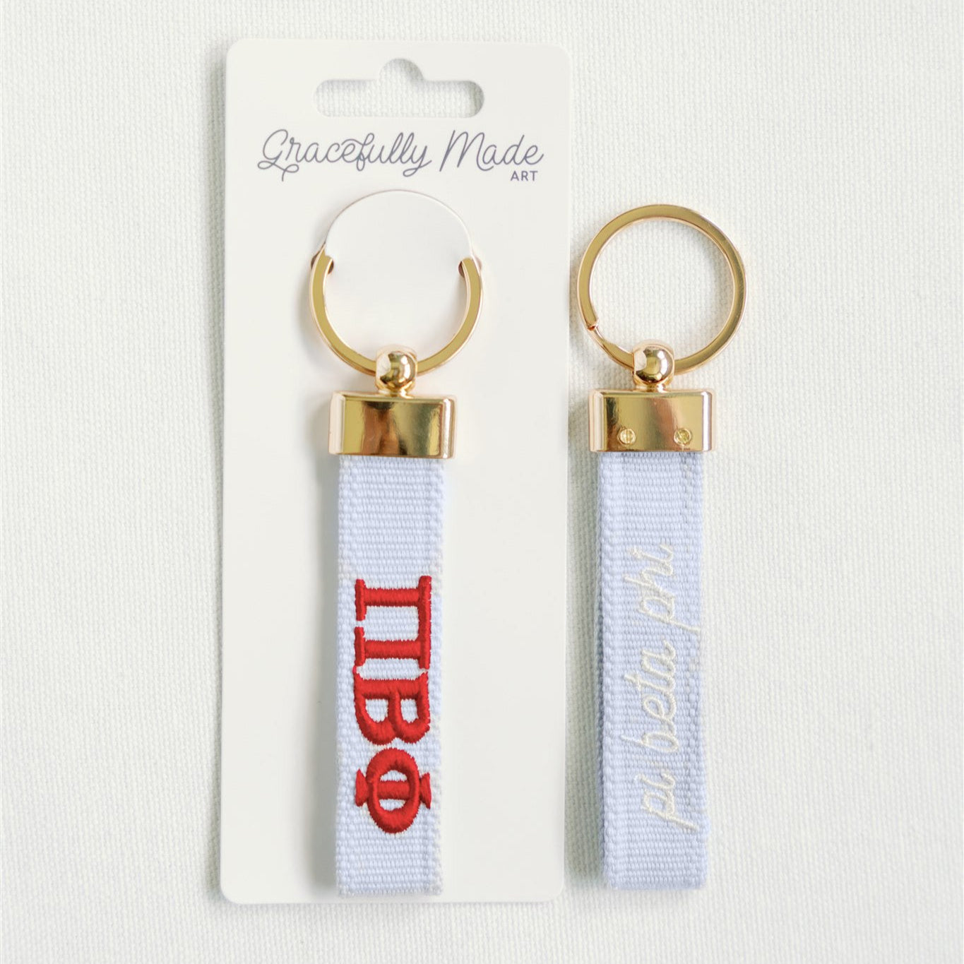 Pi Beta Phi keychain with gold loops and white ribbons featuring red text on a white background.