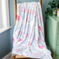 Pi Beta PHI blanket with red and blue text draped over a wooden chair in a room with a window and plant.