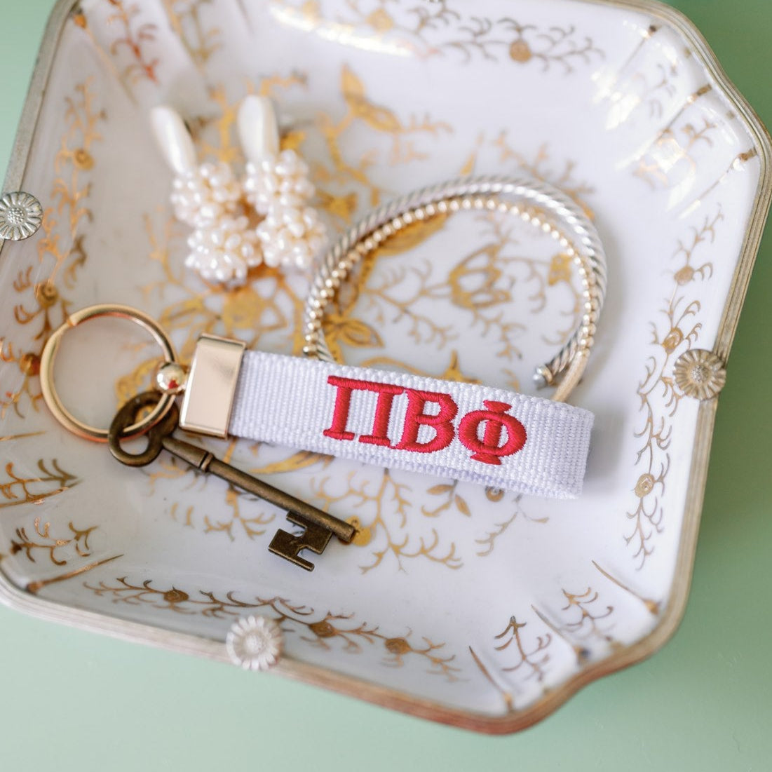 White keychain with Phi Beta Phi Greek letters embroidered in red on a decorative jewelry dish.