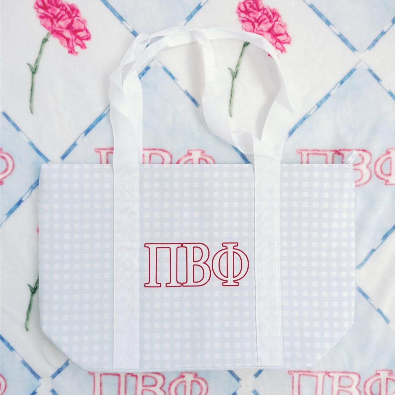 Gray checkered tote bag with Pi Beta Phi Greek letters and white straps on a patterned background.