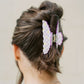 Person with a bun wearing a decorative purple and yellow hair clip on a plain background